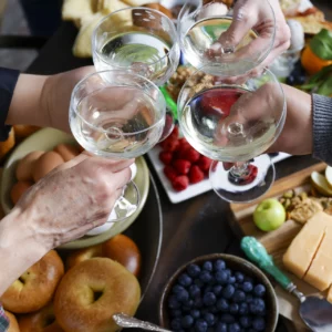 Four adults holding wine glasses around a table full of food.