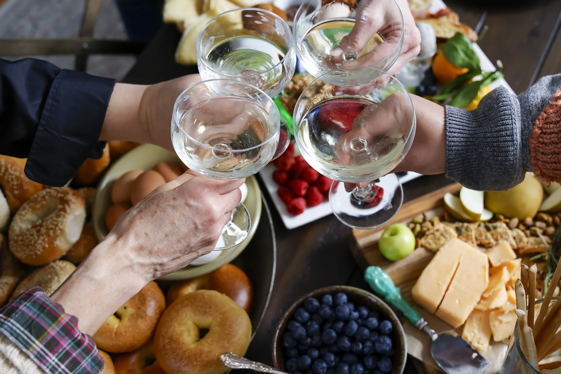 Four adults holding wine glasses around a table full of food.