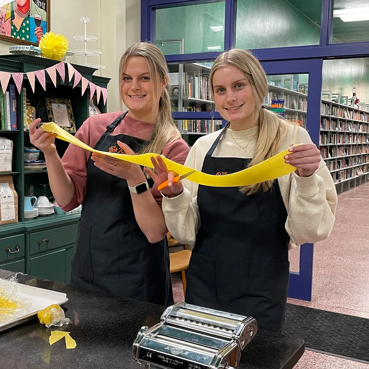 Two women holding rolled out pasta