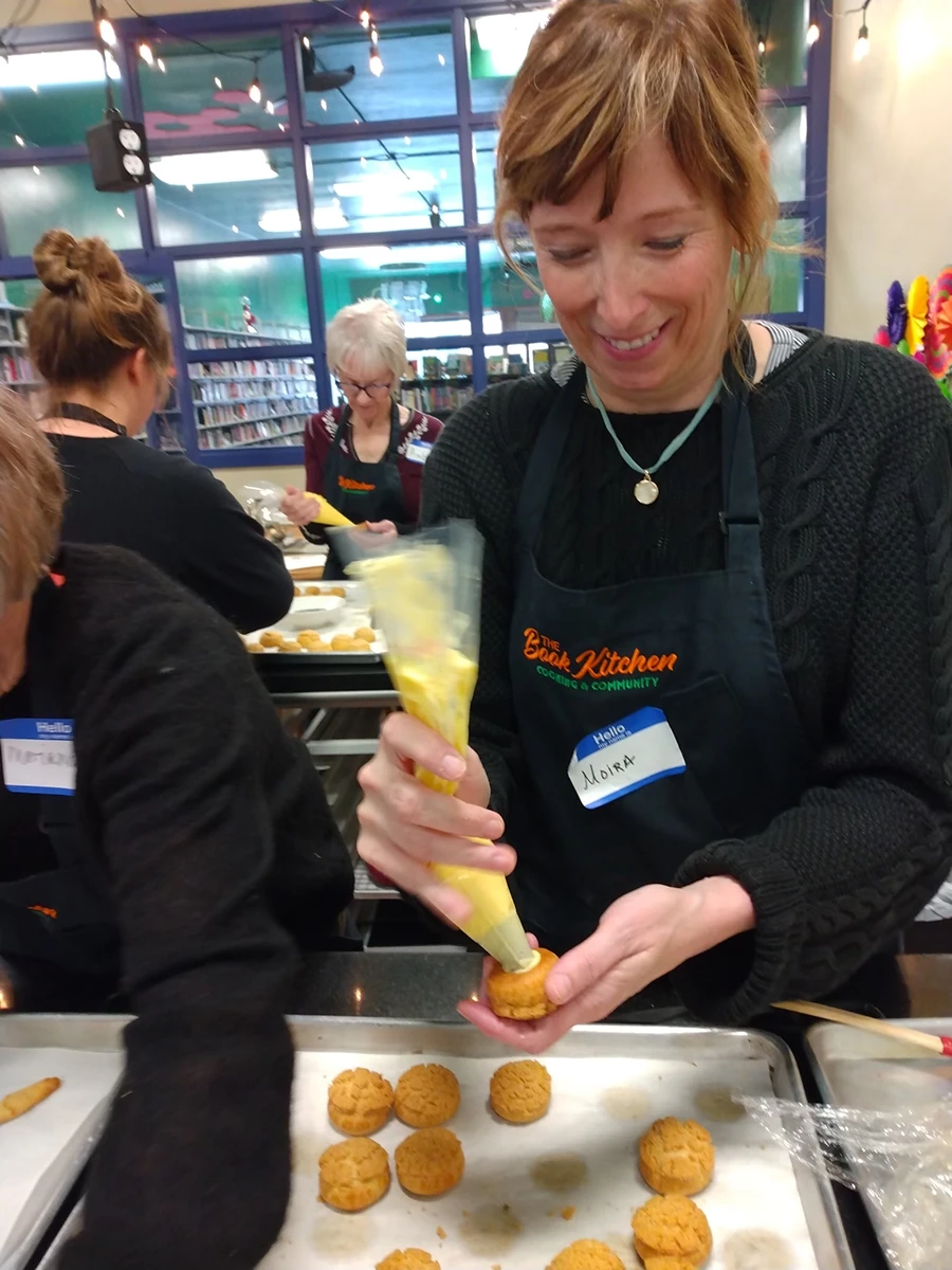 A woman piping cream inside a small pate a choiux