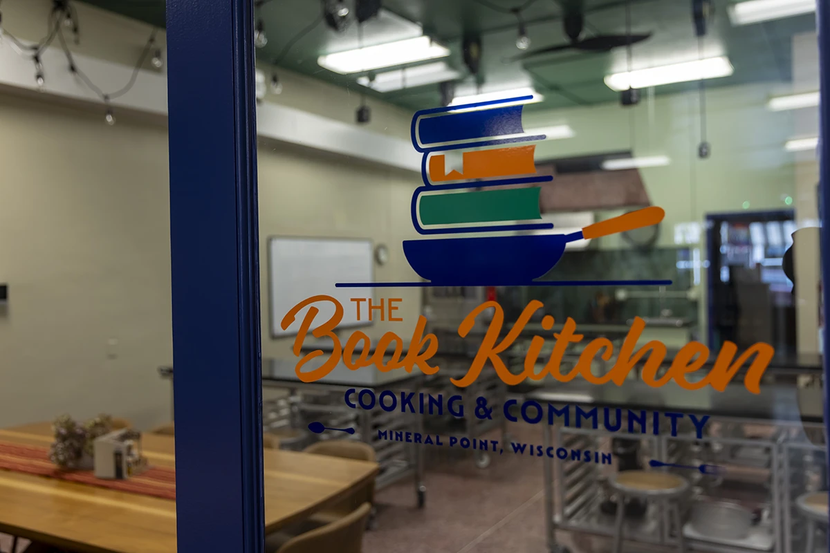 the book kitchen logo on the window with the kitchen in the back
